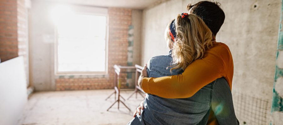 back view of an embraced couple standing at their renovating apartment. Copy space.